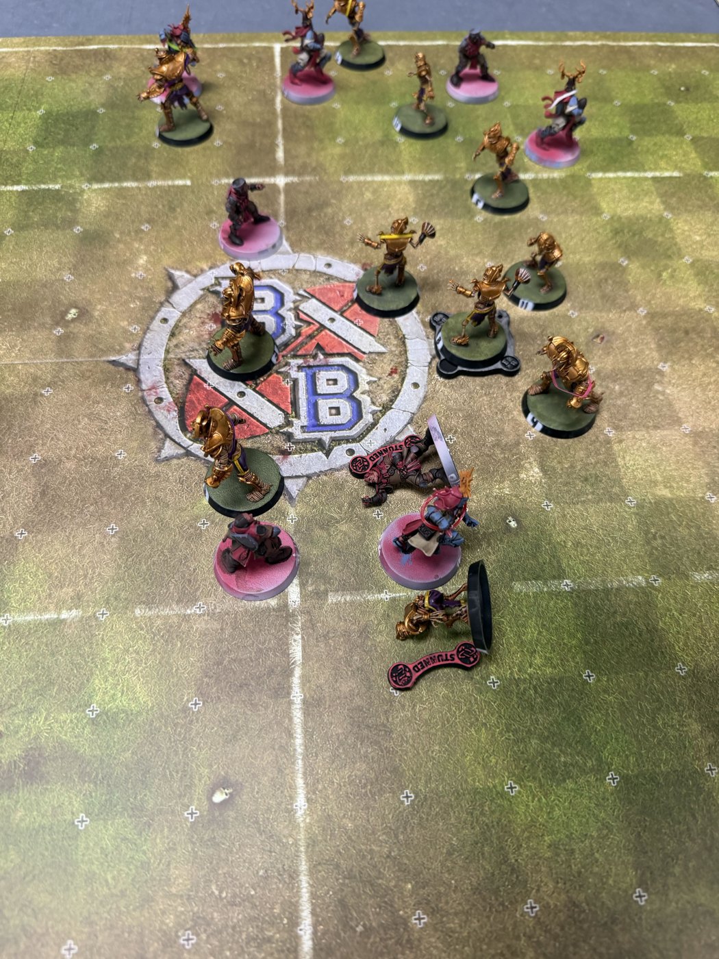 Overhead view of the scrum around the center logo, gold Tomb Kings pressing into the knights