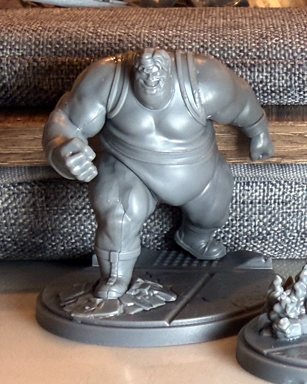Unpainted Blob mini grinning, fist clenched, standing on a cracked pavement base