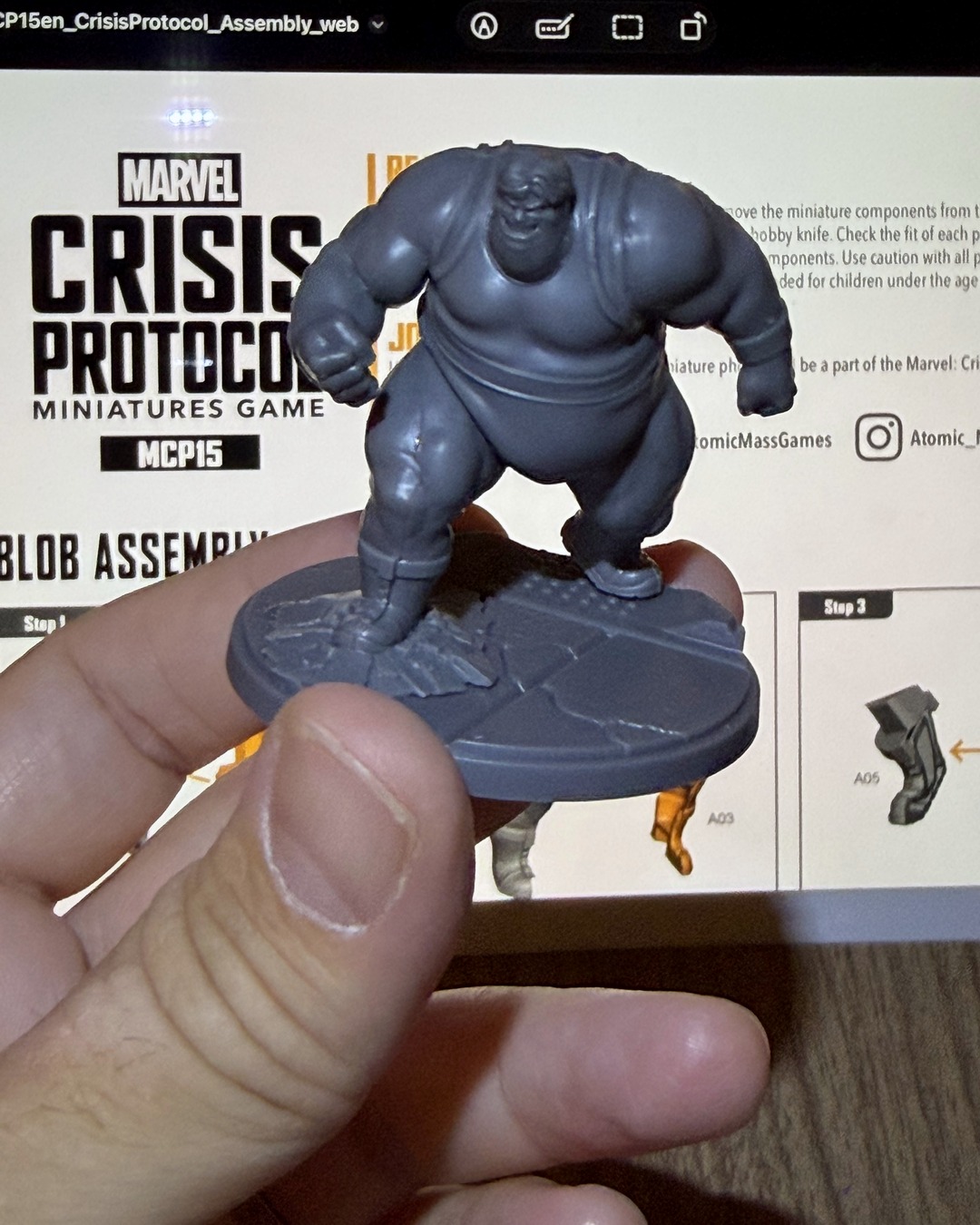 Assembled Blob held up in front of the Crisis Protocol Blob assembly guide on an iPad