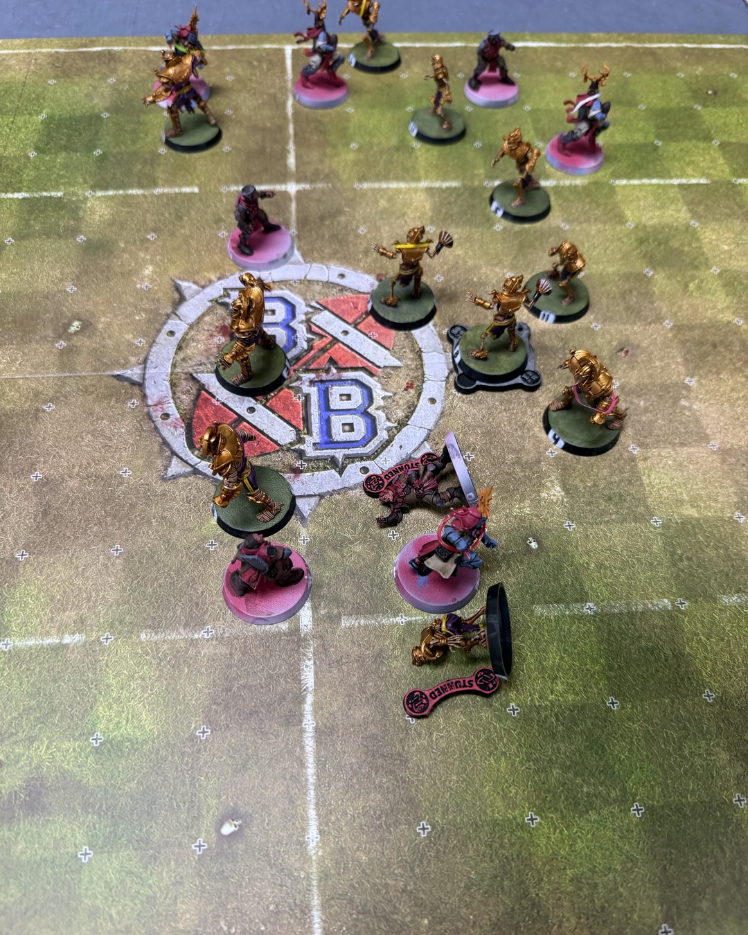 Overhead view of the scrum around the center logo, gold Tomb Kings pressing into the knights