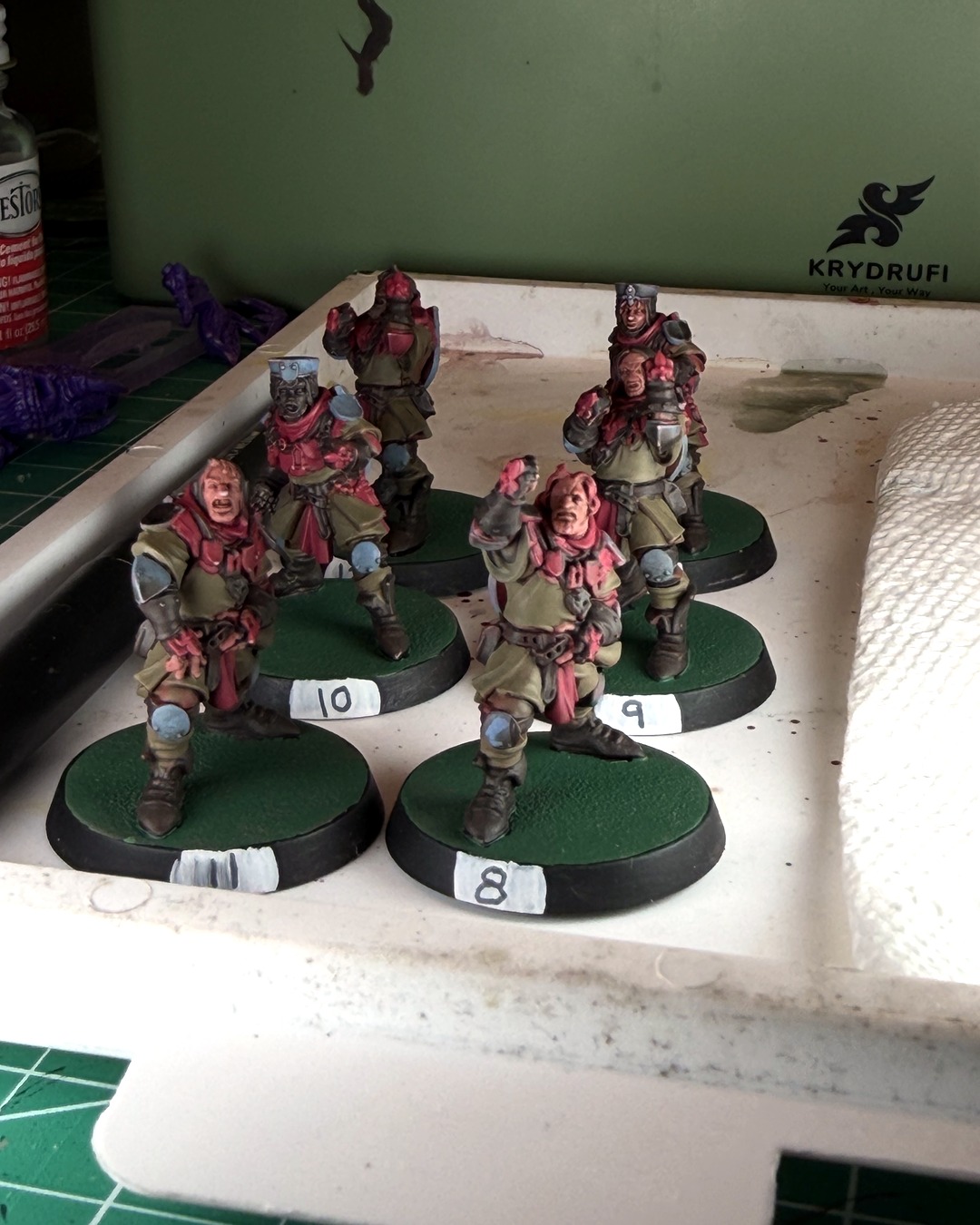 Six work-in-progress Bretonnian squires, including numbers 8 to 11, lined up in the painting station tray, Krydrufi logo on the station behind them