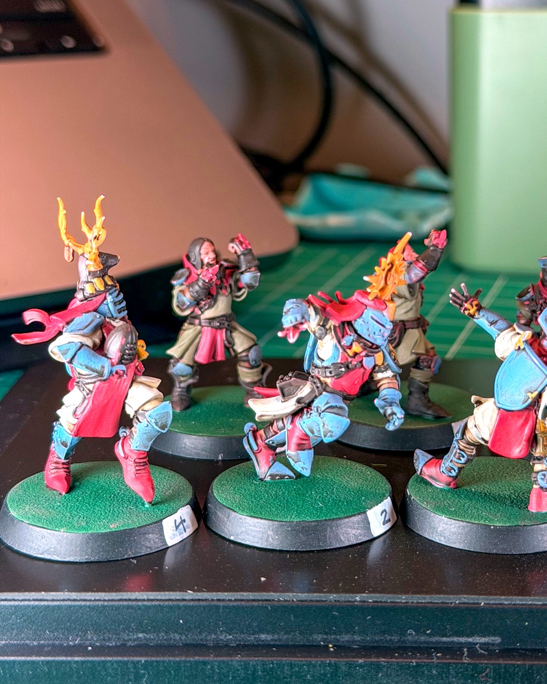 Knight number 4 in a gold antler crest and knight number 2 lunging forward, both in slate blue armor and red tabards, with squires in olive tunics behind