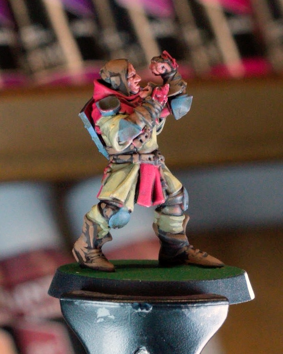 A hooded squire with fists raised, tan tunic, red tabard and blue knee pads, on a painting handle