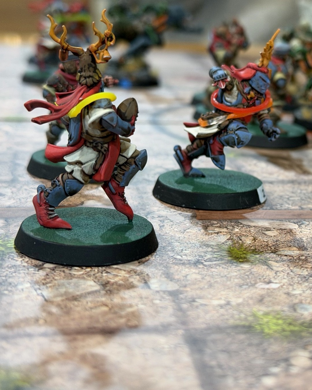 Two Grenadier knights in red and slate blue pushing upfield, the antler-crested one carrying the ball