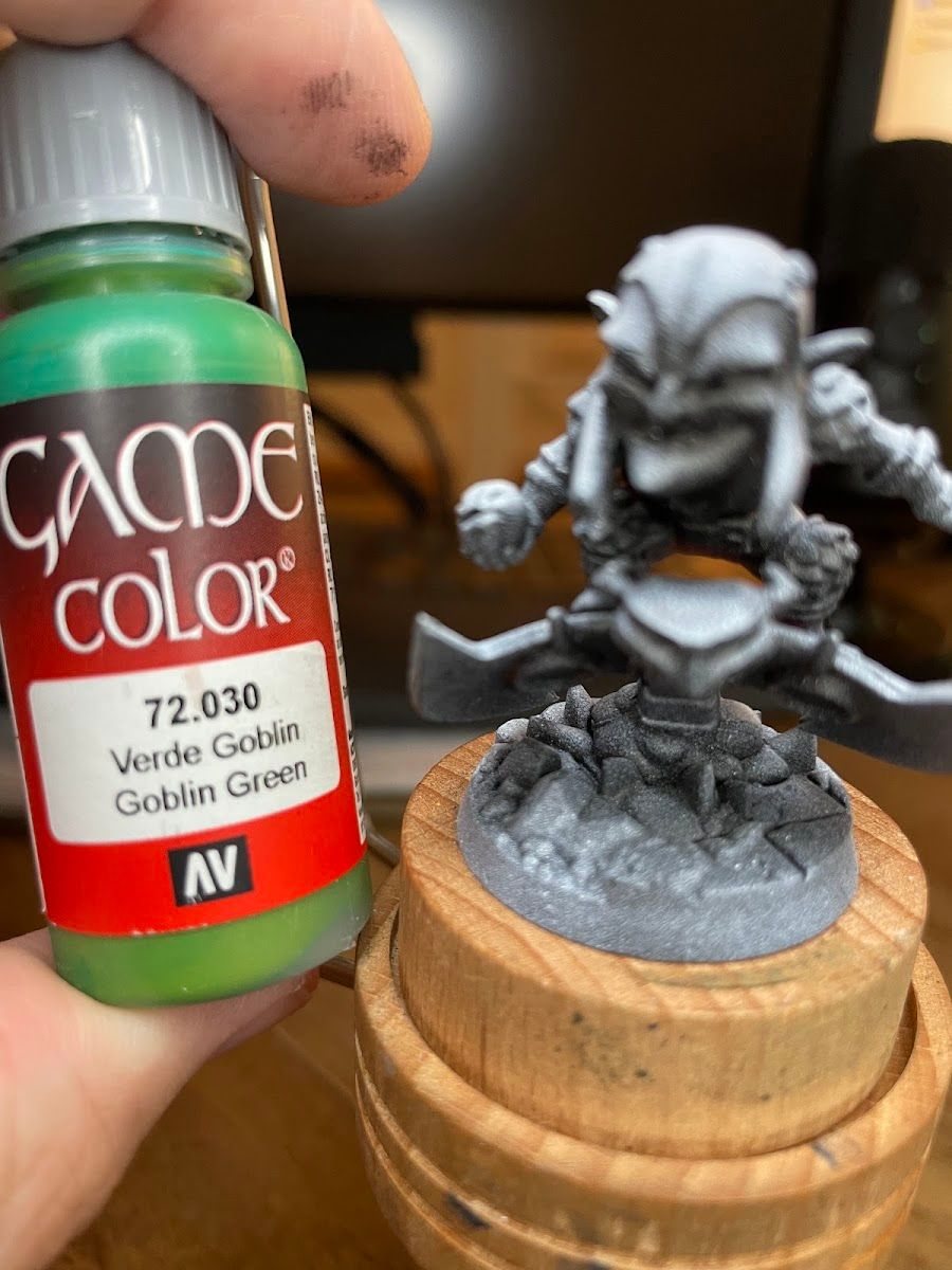 Holding a paint bottle up to a primed mini to check the color
