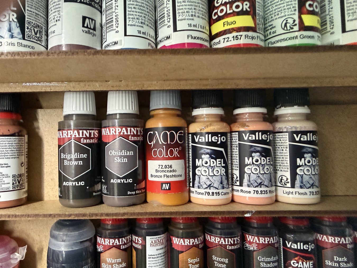 A shelf of skin tone paints from Vallejo and Army Painter, with skin shade washes on the row below