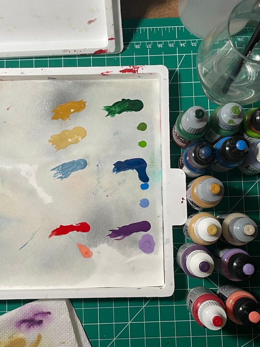 Paint bottles lined up next to a wet palette with color swatches